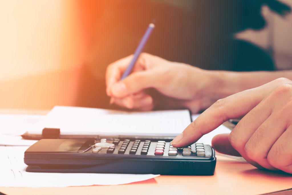 Close up young woman with calculator counting making notes at home, hand is writes in a notebook.